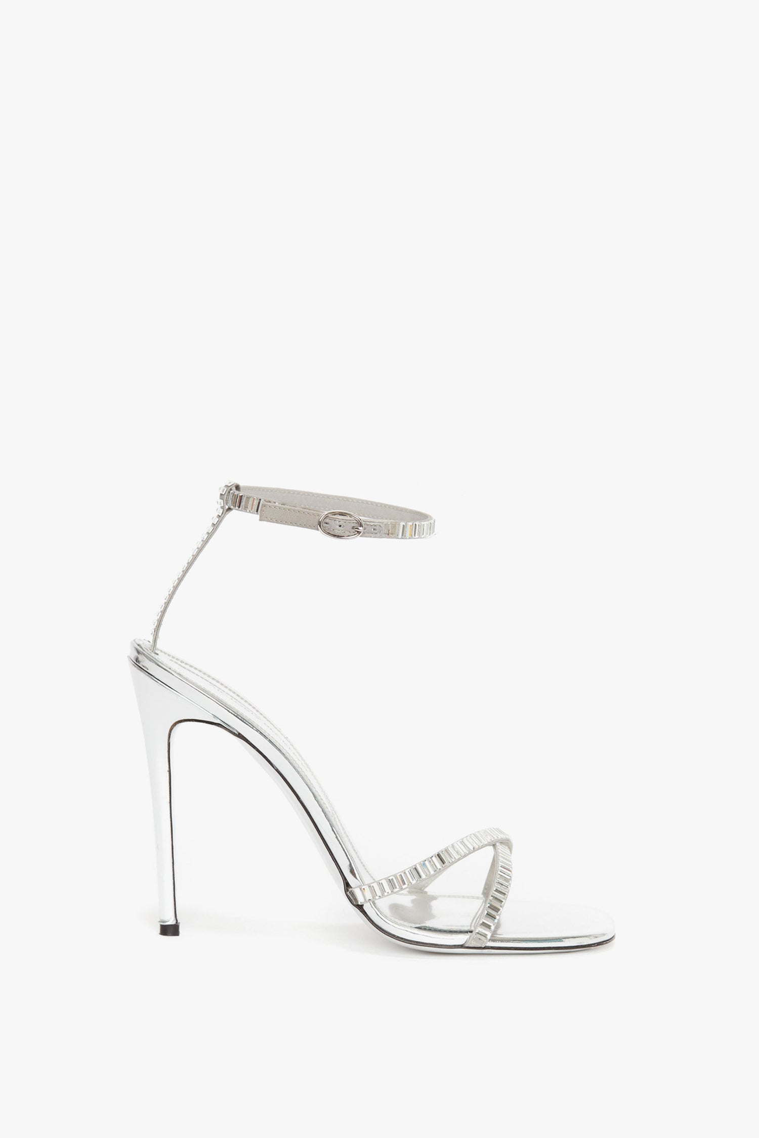 A Victoria Beckham Rhinestone Sandals In Silver made of metallic silver leather, featuring a sleek ankle strap and delicate straps across the toes, viewed from the side.
