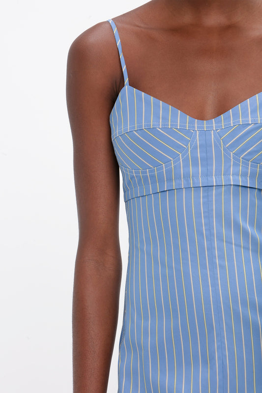 A close-up view of a person wearing the Victoria Beckham Cami Fit And Flare Midi In Steel Blue with adjustable straps, focusing on the upper torso and arm.