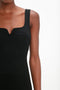 A person wearing a Victoria Beckham Sleeveless Fitted T-Shirt Dress In Black stands against a plain background. The focus is on the upper torso and arms, showcasing the stretch double wool crepe fabric and sweetheart neckline.