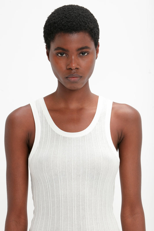 Person with short curly hair wearing a Victoria Beckham Fine Knit Vertical Stripe Tank In White, looking directly at the camera against a plain background.