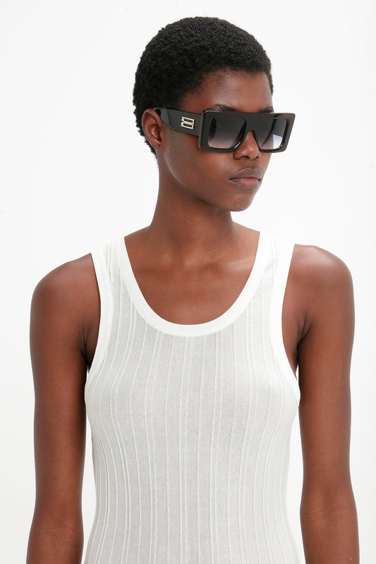 A person wearing a white ribbed tank top and Oversized Frame Sunglasses In Black from Victoria Beckham's SS24 runway collection is looking off to the side.