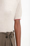 Close-up of a person wearing the Short Sleeve Top In Nougat by Victoria Beckham, paired with high-waisted khaki pants featuring two black buttons and pleats.