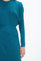 A person wearing a teal Victoria Beckham Long Sleeve Dolman Midi Dress In Petroleum, crafted from fluid cady fabric, is partially visible, with the focus on the upper body and right arm. The background is plain white, enhancing the dress's contemporary sophistication.