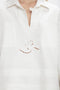 Close-up of a person wearing the Victoria Beckham Oversized Embroidered Tunic In Antique White, featuring a patterned cutout design on the front and a V-neck collar.