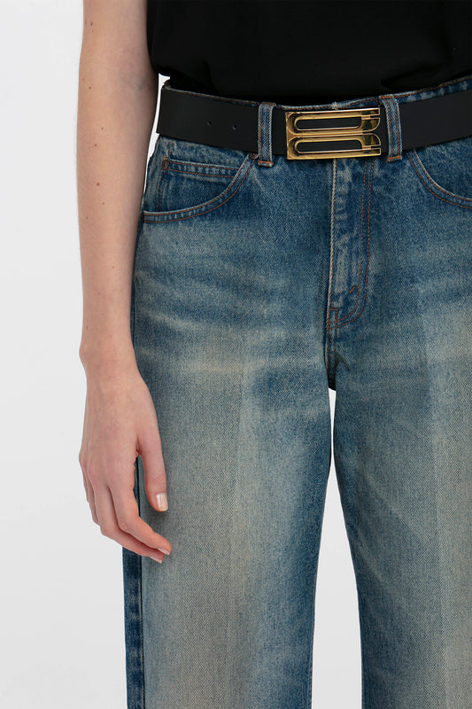 Close-up of a person wearing Victoria Beckham relaxed straight leg jeans in antique indigo wash and a black belt with a gold buckle, focusing on the midsection.