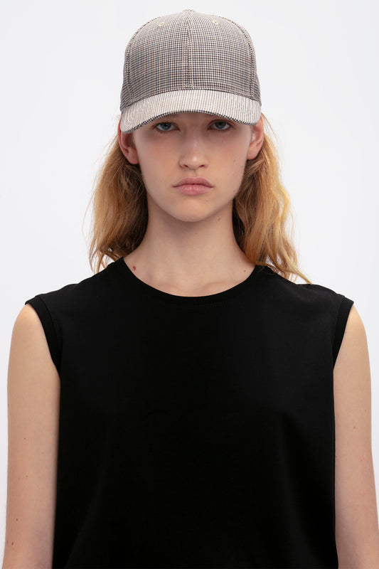 Young woman wearing a black sleeveless top and a Victoria Beckham Logo Cap In Dogtooth Check, looking directly at the camera with a neutral expression.