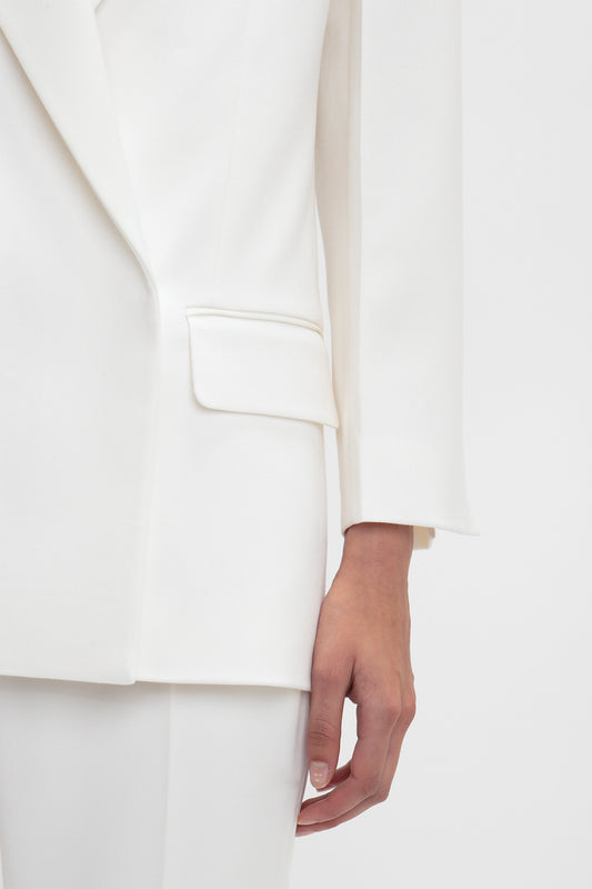 A close-up of a person wearing an Exclusive Double Breasted Tuxedo Jacket In Ivory by Victoria Beckham and white pants. The left hand, positioned near the pocket, is visible. The background is plain white.