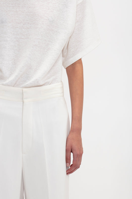 Person standing in a white semi-sheer short-sleeve shirt and Victoria Beckham Waistband Detail Straight Leg Trouser In White, with their right hand visible. The background is plain white. The upper half of the person's head is not shown, offering a minimalist take on contemporary fashion.