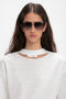 A person with long dark hair wearing V Metal Pilot Sunglasses In Grey Gradient by Victoria Beckham and a light-colored top with a small cutout near the neckline.