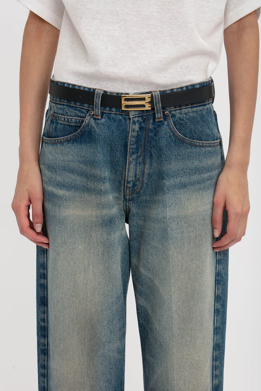 A person wearing blue jeans and a white t-shirt, with an Exclusive Frame Belt in Midnight Navy Leather crafted from calf leather featuring a gold buckle, standing with hands by their sides by Victoria Beckham.