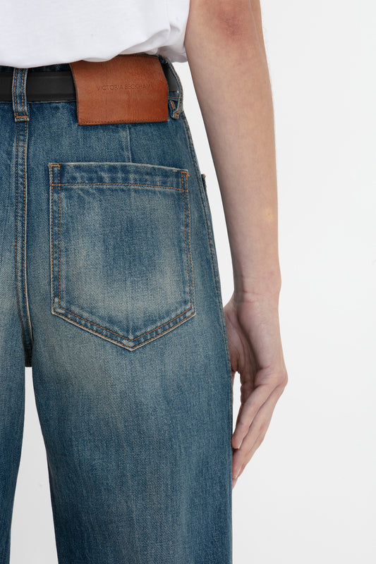 Close-up of a person wearing Victoria Beckham's Alina Jean in indigrey wash, styled with a brown leather belt. Focus on the back pocket and belt area.