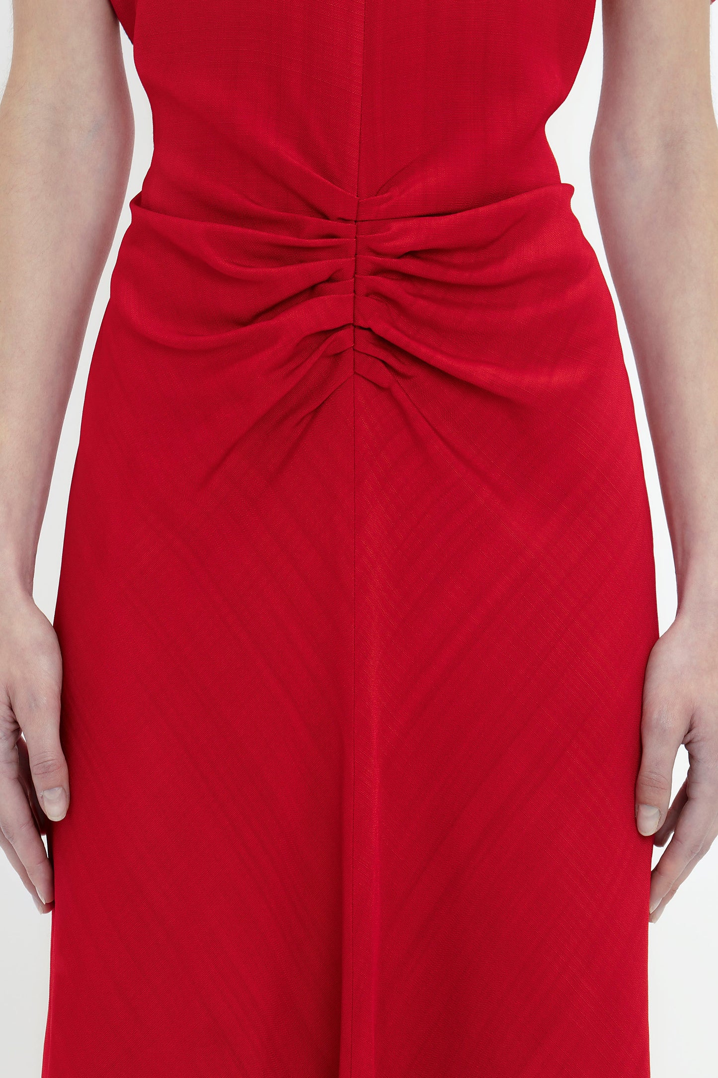 Close-up of a person wearing a red Exclusive Gathered Waist Midi Dress In Carmine by Victoria Beckham, with ruched detailing around the waist, arms resting by sides.