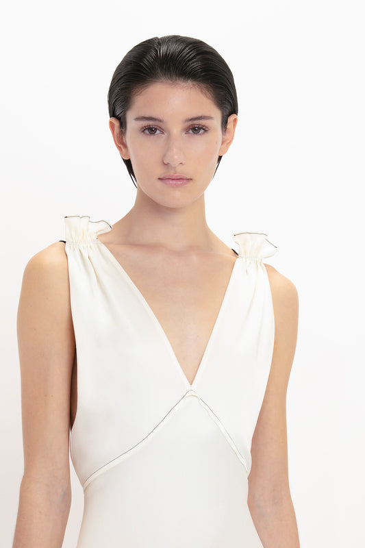 Person with short dark hair wearing a Victoria Beckham Gathered Shoulder Floor-Length Cami Gown In Ivory with feminine frills, posing against a plain white background.