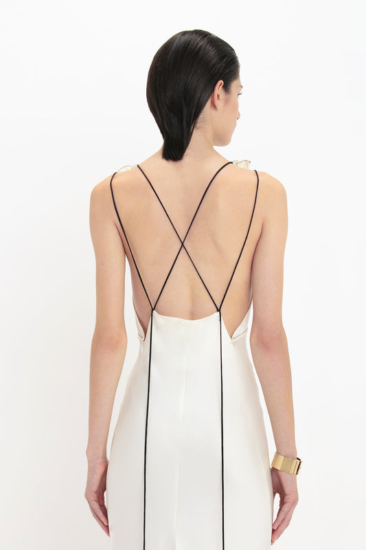 A person with slicked-back hair wearing a Victoria Beckham Gathered Shoulder Floor-Length Cami Gown In Ivory with thin black straps, viewed from behind against a plain white background.