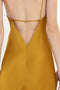 Close-up of the back of a person wearing a Victoria Beckham Low Back Cami Floor-Length Dress In Harvest Gold with thin straps and a deep V-cut, reminiscent of a 1990s camisole-slip dress.