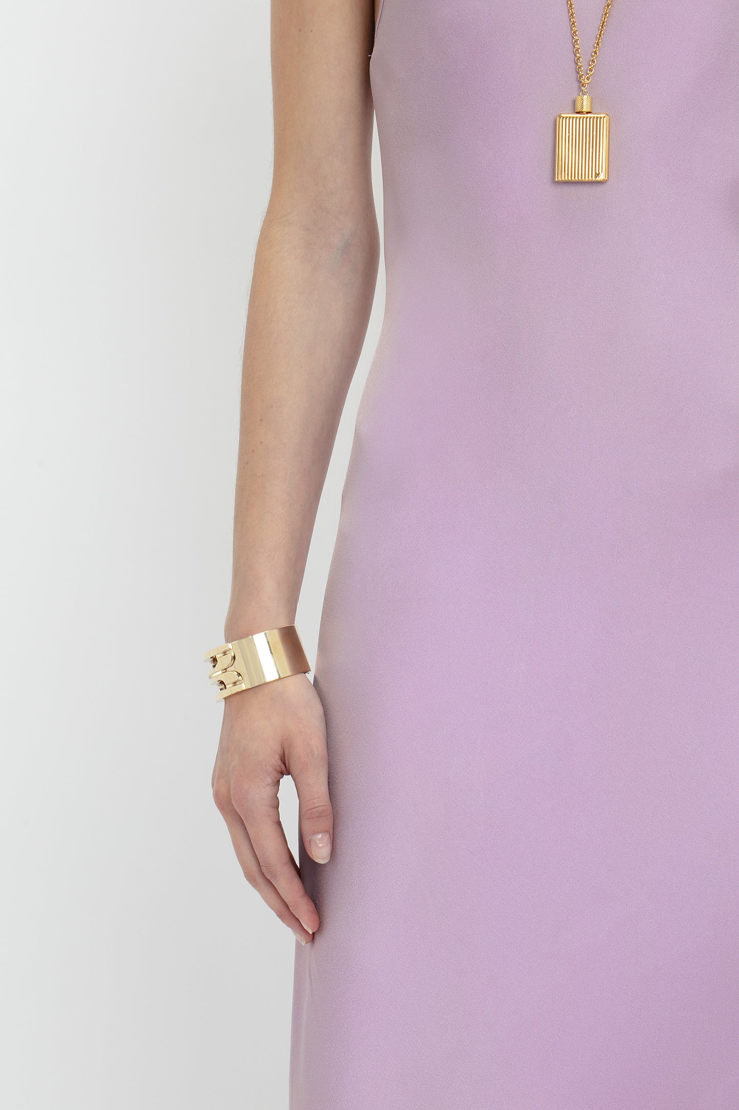 Person wearing a sleeveless, Victoria Beckham Low Back Cami Floor-Length Dress In Rosa with a sensuous silhouette, complemented by a gold bracelet and a gold pendant necklace against a plain white background.