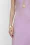 Person wearing a sleeveless, Victoria Beckham Low Back Cami Floor-Length Dress In Rosa with a sensuous silhouette, complemented by a gold bracelet and a gold pendant necklace against a plain white background.