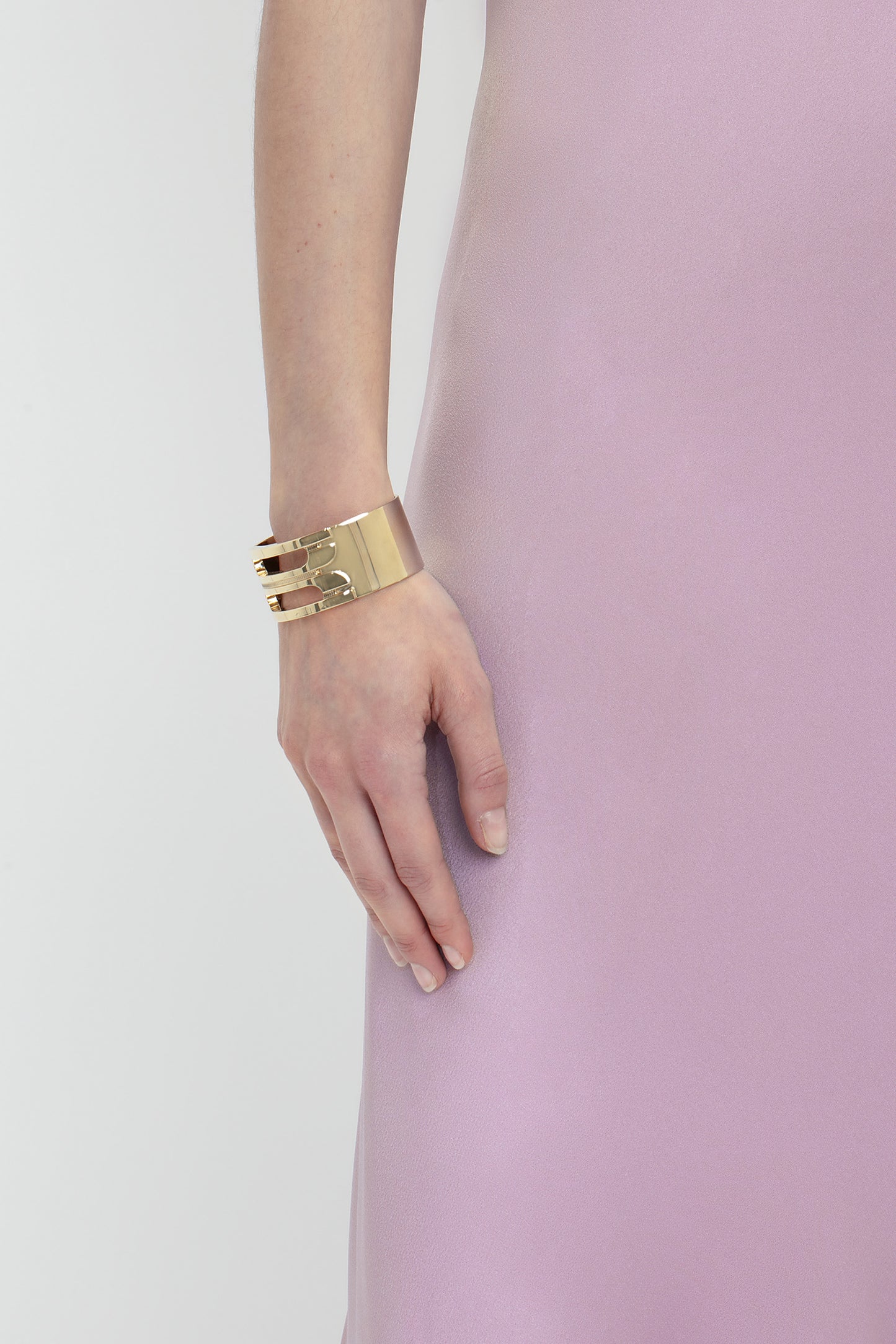 A person wearing a gold bracelet and a Low Back Cami Floor-Length Dress In Rosa by Victoria Beckham is shown from the torso down with their hand resting by their side, highlighting a sensuous silhouette.