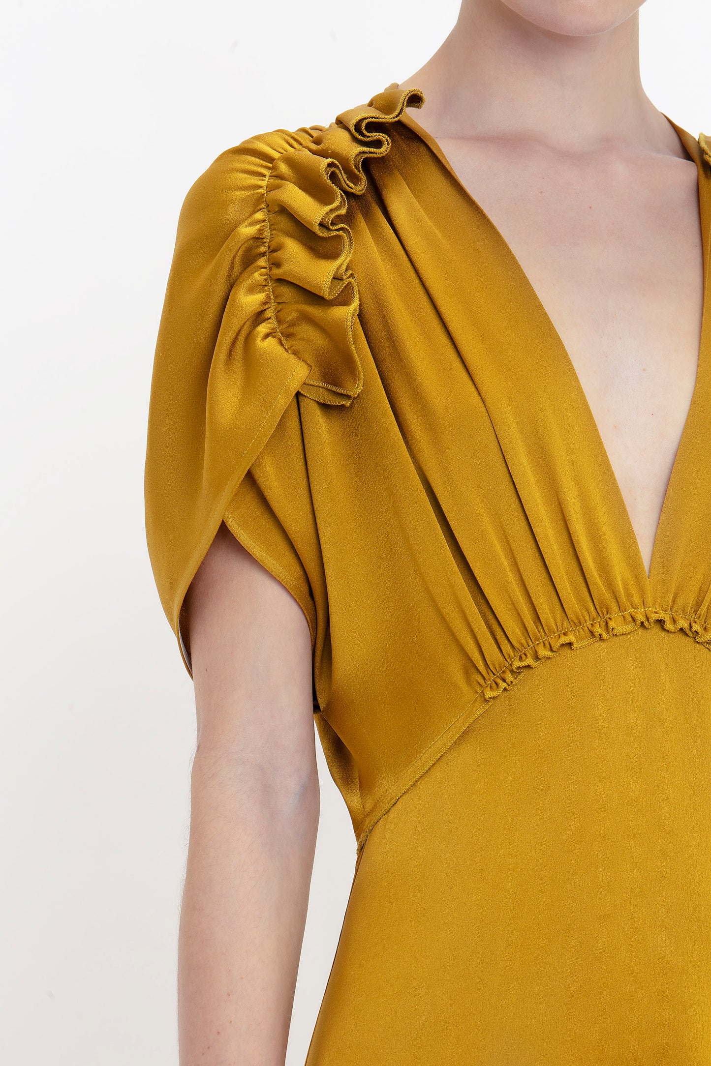 Close-up of a person wearing a Harvest Gold dress with shoulder frills and a deep V-neckline. The image shows only the upper part of this Victoria Beckham V-Neck Ruffle Midi Dress In Harvest Gold from the neck to the upper waist.