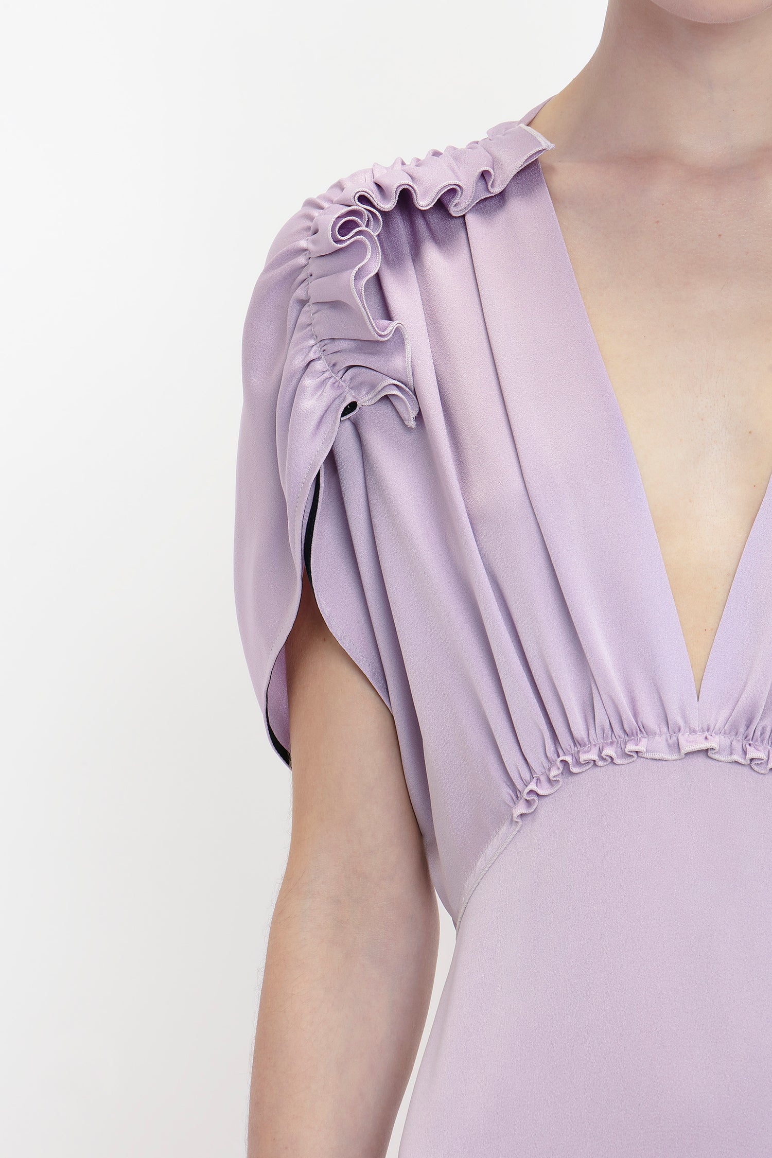 Close-up of a person wearing a V-Neck Ruffle Midi Dress In Petunia with ruffled shoulders and deep V-neckline. The Victoria Beckham brand dress fabric appears soft and has gathered detailing below the shoulder, epitomizing elegant dresses.