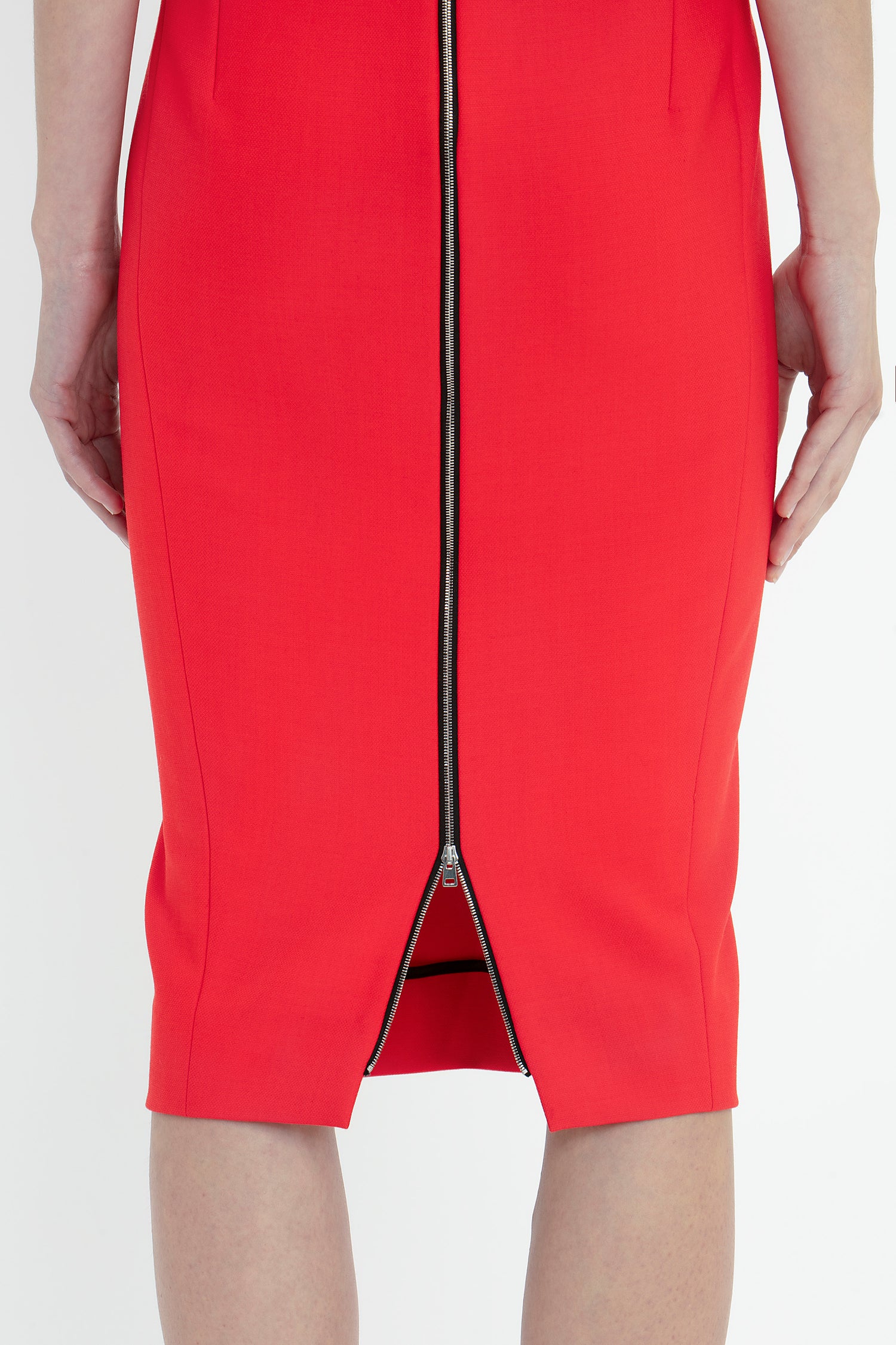 A person wearing a Victoria Beckham Sleeveless Fitted T-Shirt Dress In Bright Red with a visible back zipper stands with arms at their sides, showing the lower half of the dress from behind.