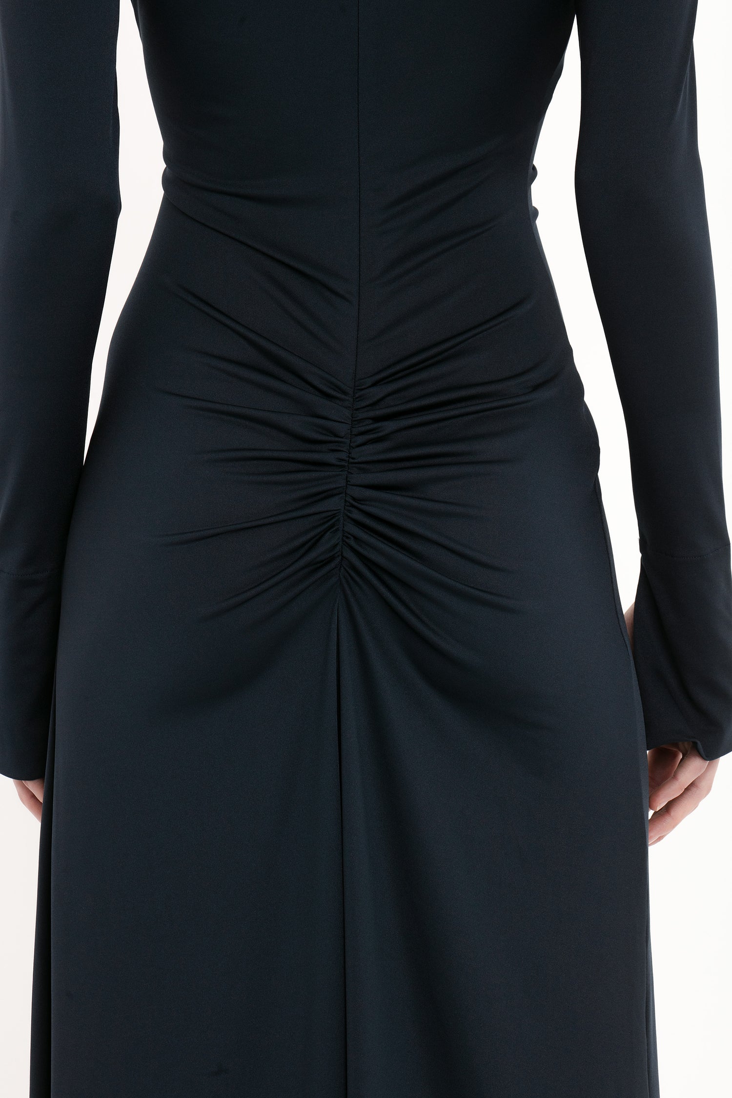 A close-up image of a person wearing a Ruched Detail Floor-Length Gown In Midnight by Victoria Beckham, with gathered and ruched detail at the back, creating a central focal point. The fabric appears to be dark and smooth, embodying understated glamour.