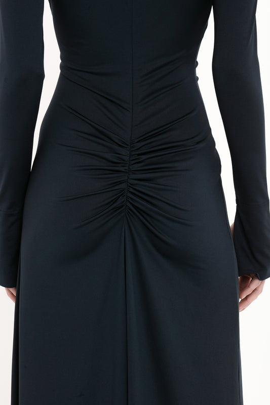 A close-up image of a person wearing a Ruched Detail Floor-Length Gown In Midnight by Victoria Beckham, with gathered and ruched detail at the back, creating a central focal point. The fabric appears to be dark and smooth, embodying understated glamour.