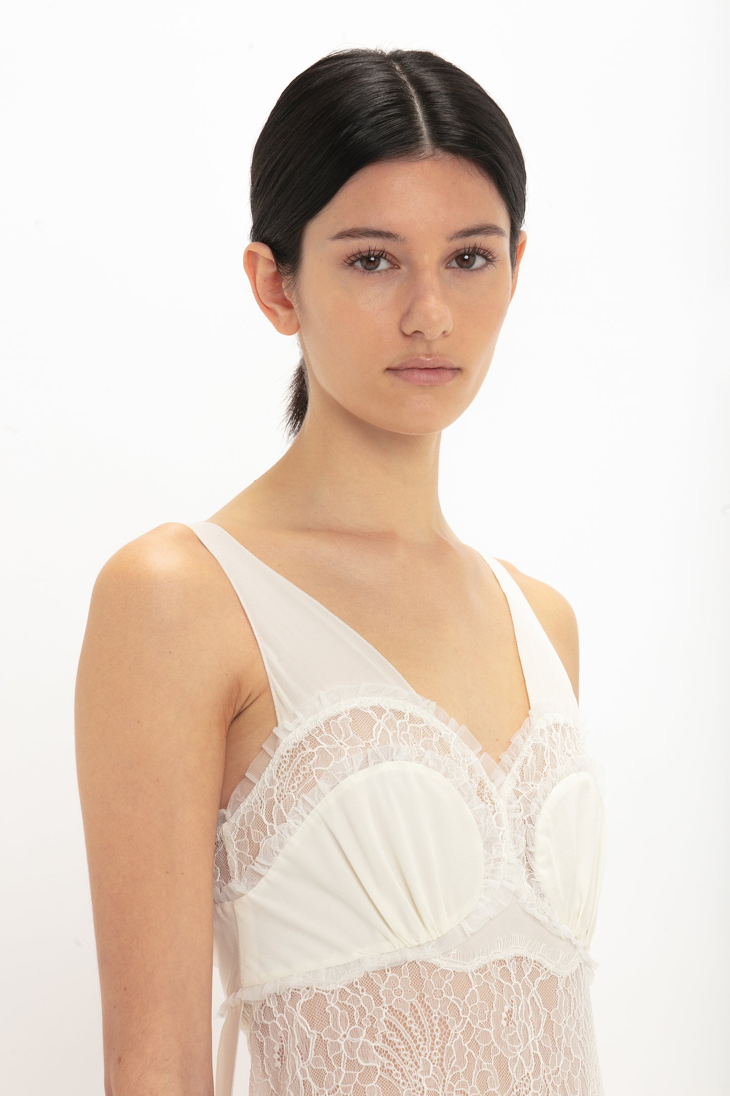 A person with dark hair is wearing a Victoria Beckham Ruffle Detail Midi Dress In Ivory, looking towards the camera against a plain white background.
