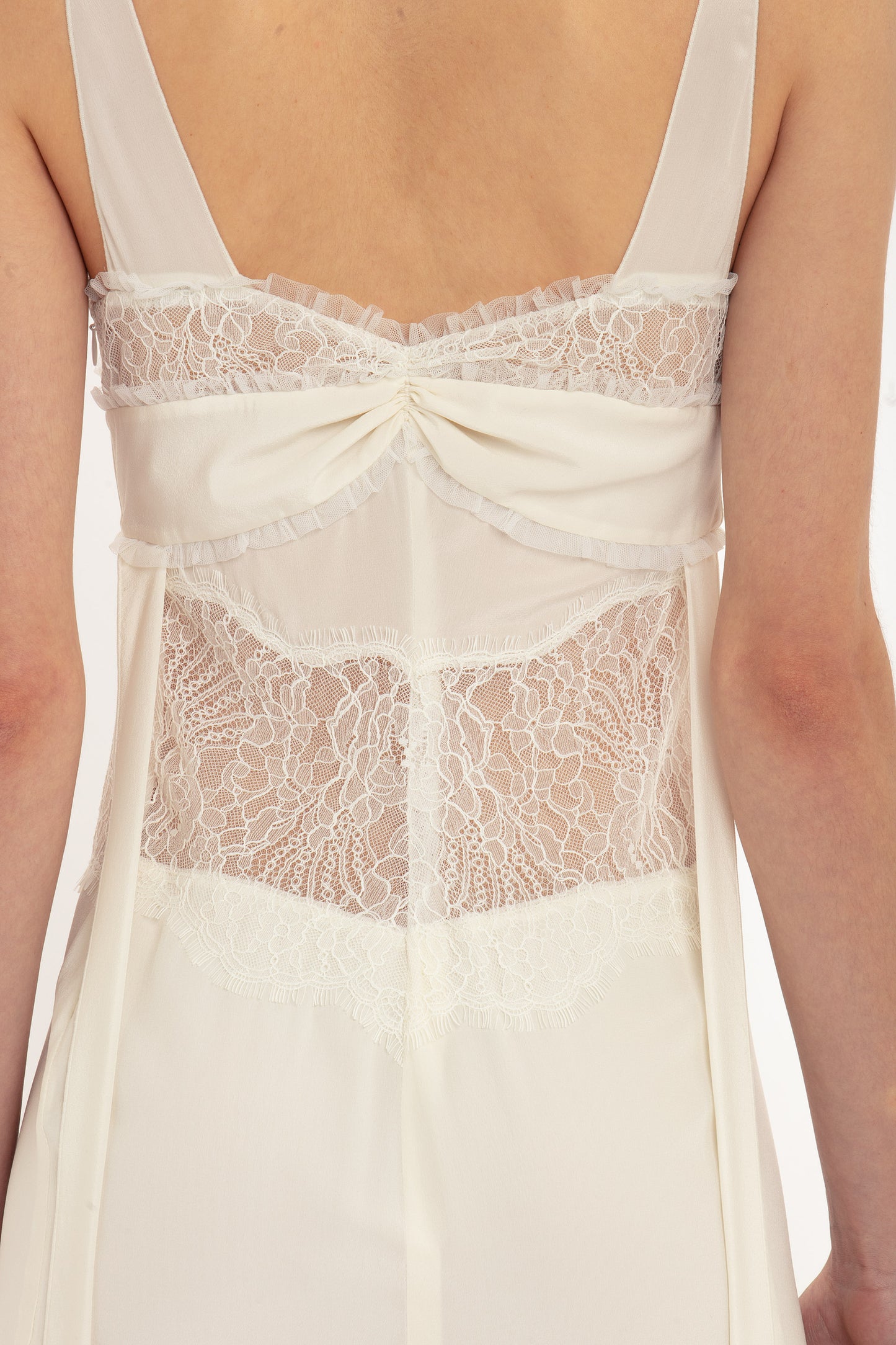 Back view of a person wearing the Victoria Beckham Ruffle Detail Midi Dress In Ivory, adorned with tactile lace and a decorative bow on the upper back.