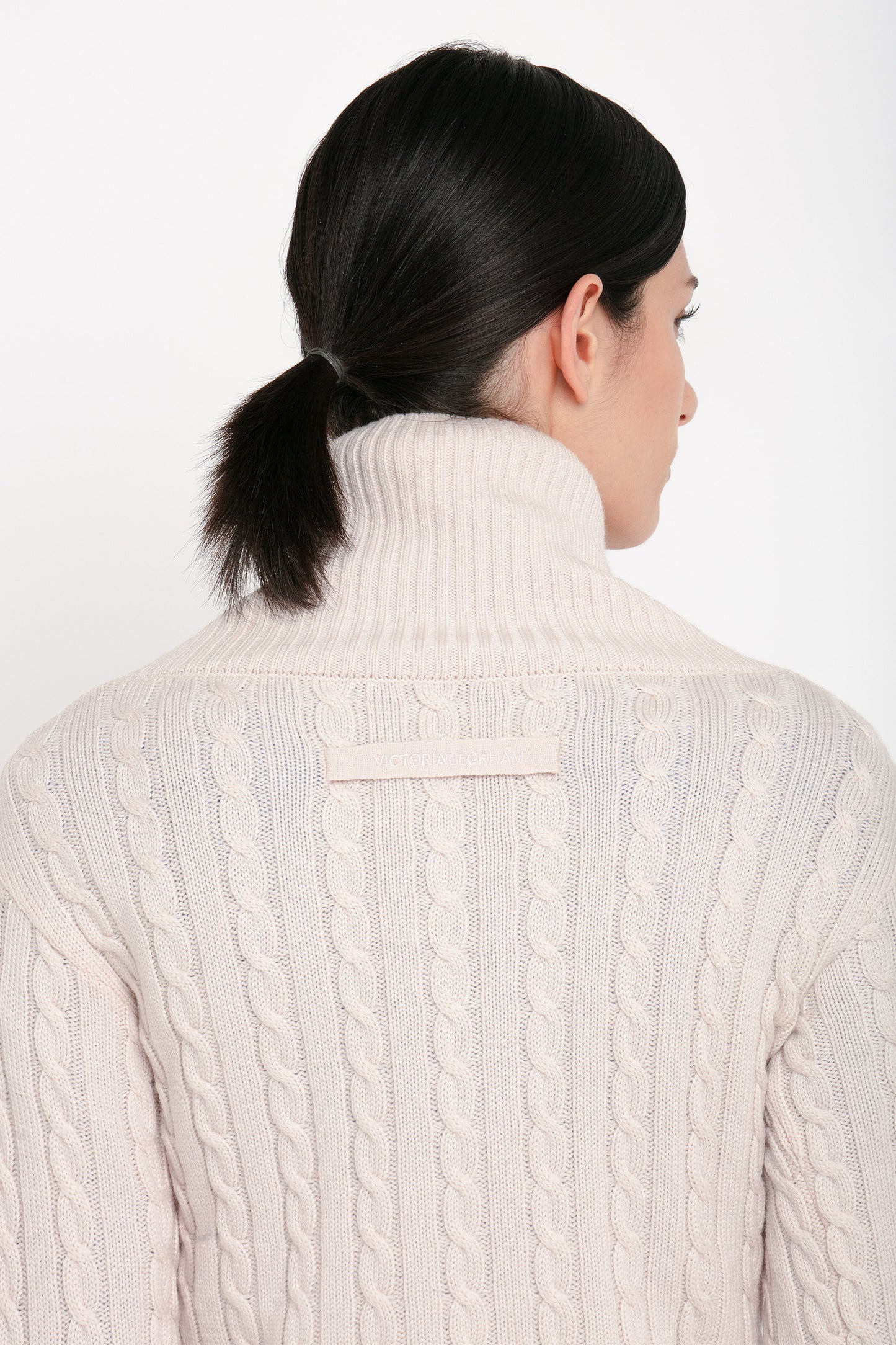 A person with dark hair in a low ponytail is seen from the back, wearing the Victoria Beckham Wrap Detail Jumper In Bone.