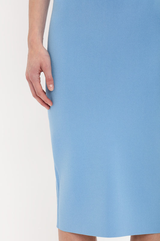 Close-up of a person's hand resting beside their Fitted Midi Skirt In Marina by Victoria Beckham, tailored with contemporary polish and made from compact knit fabric, against a plain background.