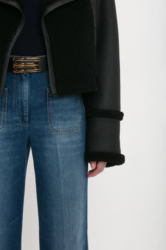 Person wearing the Victoria Beckham Shearling Jacket In Black, a black top, and blue high-waisted jeans with front pockets.
