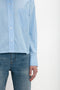 A person wearing a Victoria Beckham Cropped Long Sleeve Shirt In Marina-White, paired with jeans, is standing against a plain white background. Only the upper half of the body and part of the arm are visible.