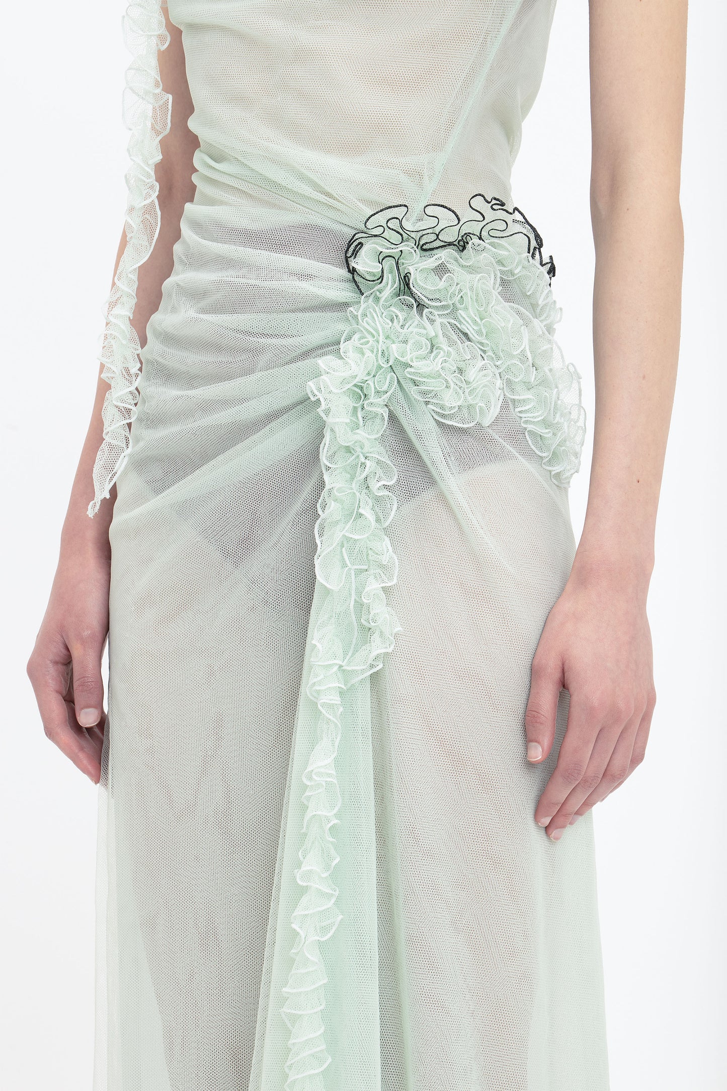 A close-up of a person wearing a Gathered Tulle Detail Floor-Length Dress In Jade by Victoria Beckham, with sheer ruched details and a black accent at the waist. The image shows the ethereal gown from shoulder to mid-thigh, reminiscent of something you might find on VictoriaBeckham.com.