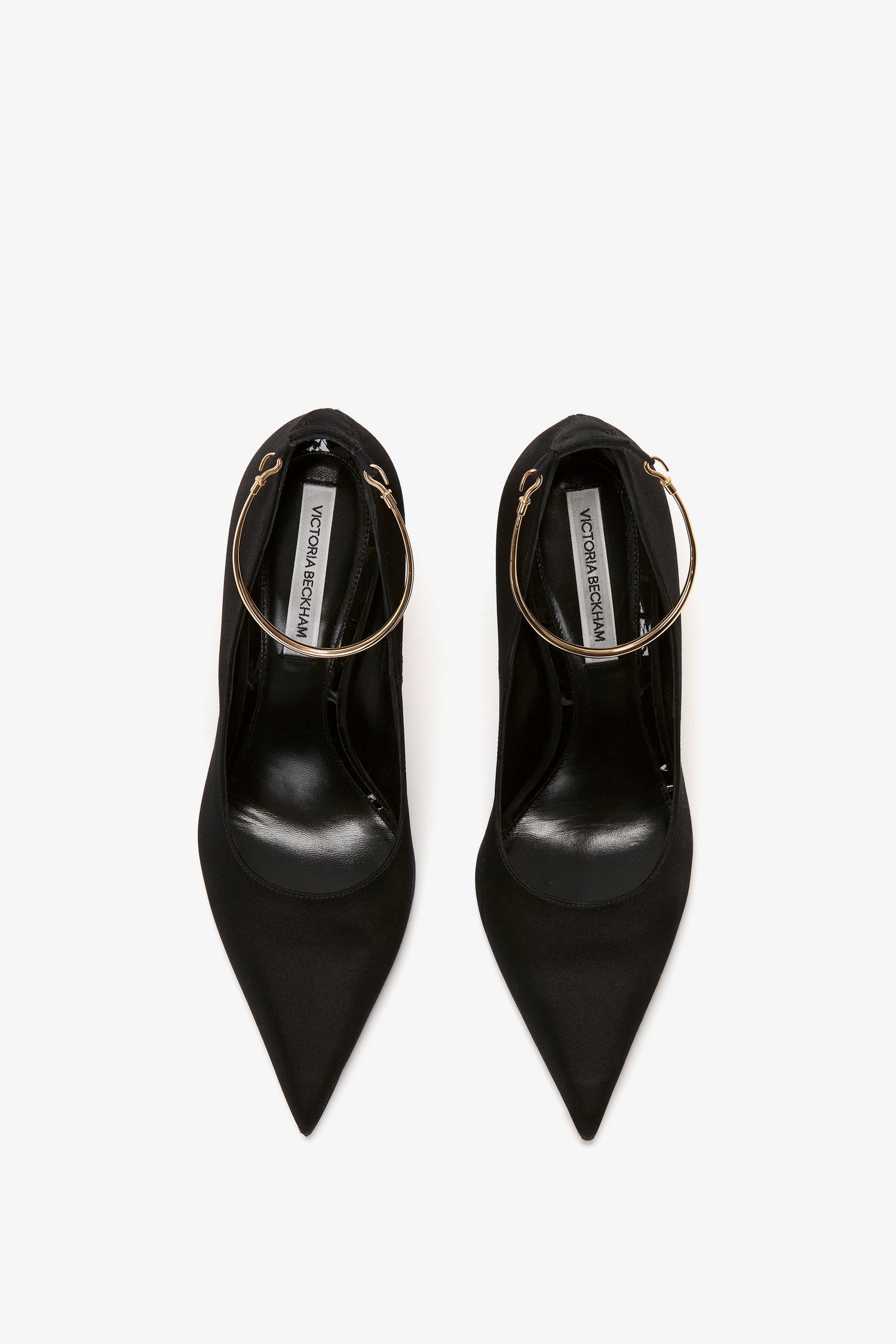 A pair of Victoria Beckham Pointy Toe Pump in Black Satin with gold hoop ankle straps, featuring a sleek 100mm heel, viewed from above.