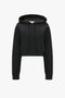 Victoria Beckham Cropped Neoprene Hoodie In Black with long sleeves and a drawstring hood, displayed against a plain white background.