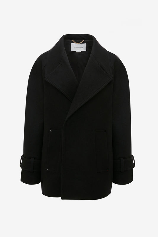 Black, long-sleeve double-breasted oversized pea coat with wide lapels, front pockets, and buckled straps on the cuffs, made from luxurious melton wool. The Victoria Beckham Oversized Pea Coat In Black hangs elegantly on an invisible hanger against a plain white background, showcasing its impeccable masculine tailoring.