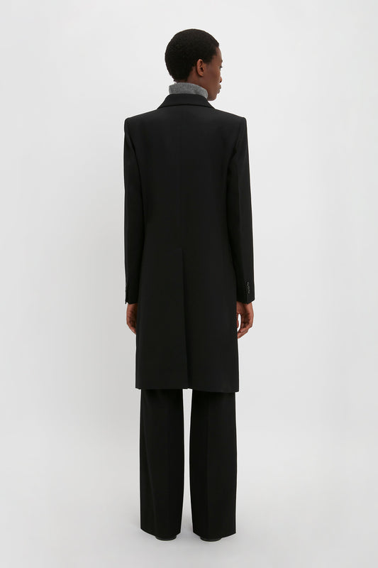 A person dressed in a slim fit Double Breasted Tuxedo Coat in Black by Victoria Beckham and black pants stands facing away against a plain white background.