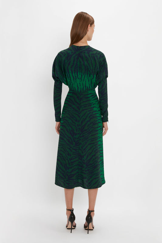 Rear view of a woman wearing a Victoria Beckham Dolman Midi Dress In Green-Navy Tiger Print with long sleeves, standing against a white background.