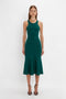 A woman stands against a white background wearing a flattering flared silhouette, teal-colored VB Body Sleeveless Dress In Lurex Green with black high-heeled sandals, perfect for updating your new-season wardrobe by Victoria Beckham.