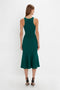 A woman with long brown hair is wearing a sleeveless, green VB Body Sleeveless Dress In Lurex Green from Victoria Beckham's new-season wardrobe, standing with her back facing the camera. She is also wearing black high heels.