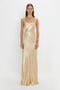 A person is standing against a plain white background, wearing the Victoria Beckham Exclusive Floor-Length Cami Dress In Gold.