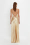 A woman is seen from the back wearing an Exclusive Floor-Length Cami Dress In Gold by Victoria Beckham. The golden gown complements her straight, shoulder-length hair.