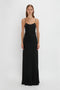 A person stands against a plain white background wearing the Floor-Length Cami Dress In Black by Victoria Beckham, crafted from elegant crepe back satin.