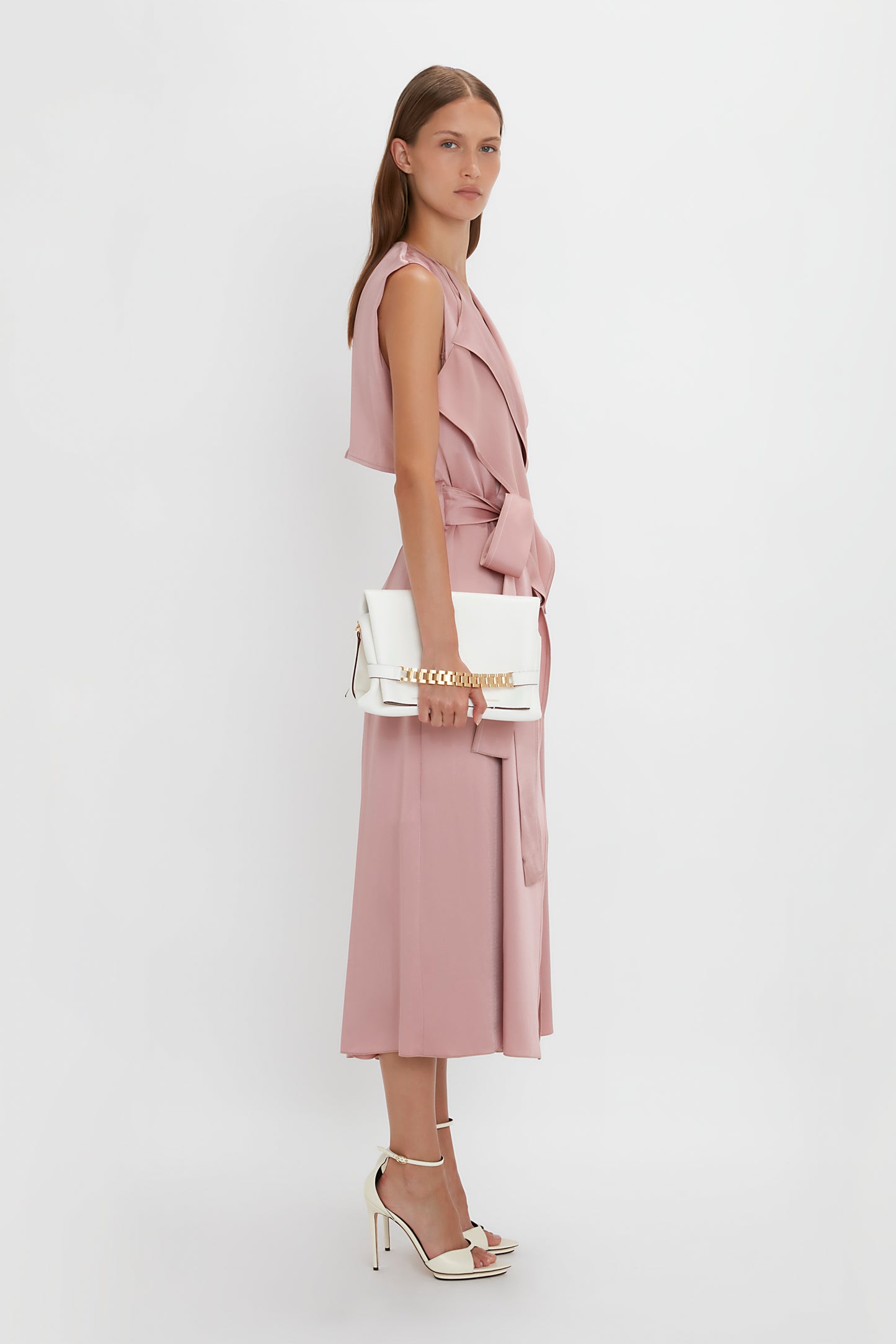 Woman in a pink sleeveless dress with a white Victoria Beckham Nappa leather Chain Pouch with Strap, standing against a plain white background.
