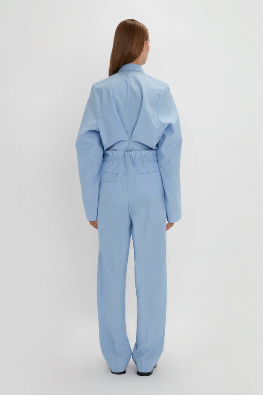 A person with long hair, seen from behind, is wearing an Oxford Blue oversized suit with long sleeves and a matching pair of Gathered Waist Utility Trousers in Oxford Blue by Victoria Beckham, embodying a modern take on utility wear against a plain white background.