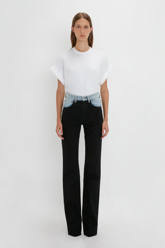 A woman in a white t-shirt and high waist black Julia Jean In Contrast Wash jeans standing against a white background by Victoria Beckham.