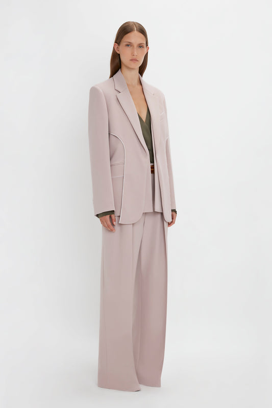 A person with straight brown hair is wearing a Victoria Beckham Double Panel Front Jacket In Rose Quartz and matching wide-legged pants paired with a dark green top. They stand against a plain white background.