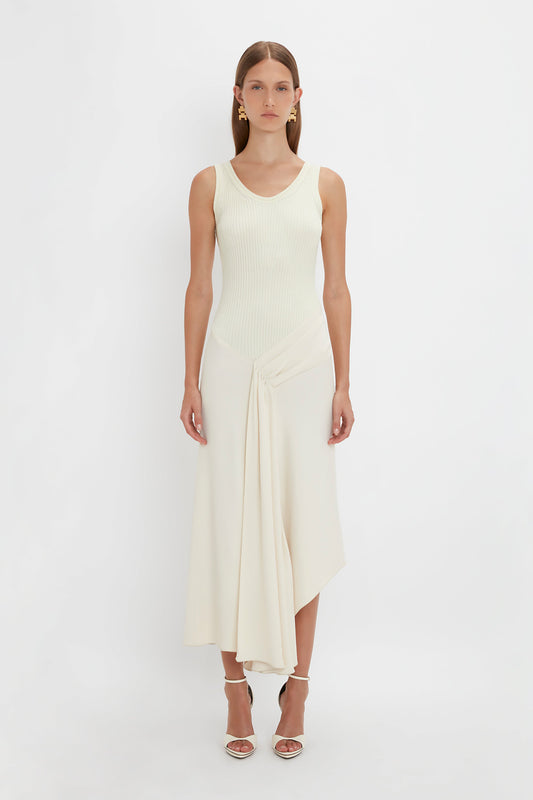 A person stands against a white background wearing the Sleeveless Tie Detail Dress In Cream by Victoria Beckham, paired with strappy heels.