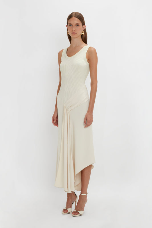 A woman wearing the Sleeveless Tie Detail Dress In Cream by Victoria Beckham pairs it perfectly with white high-heeled sandals, standing against a plain white background.